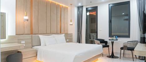 A modern hotel room with a large bed, bedside tables, a desk, a chair, and a view of the outside.