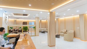 A modern hotel lobby with a reception desk, seating area, and a large plant.