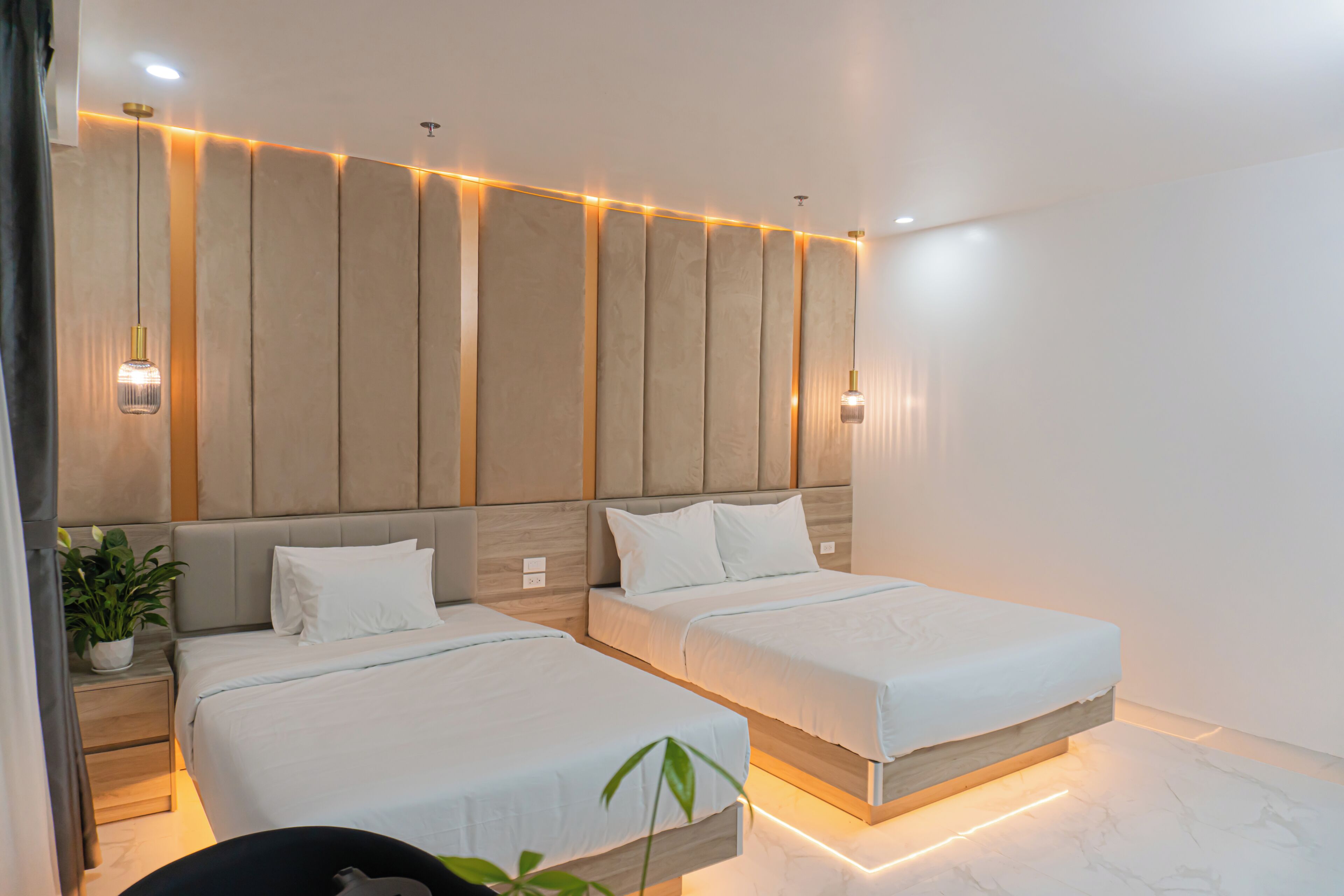 Ein modernes Hotelzimmer mit zwei Betten, einem Kopfteil mit vertikalen Paneelen, Nachttischlampen und einem Blumentopf.