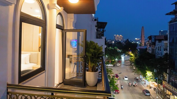 A hotel balcony with a view of the city street, a potted plant, and a lit interior.