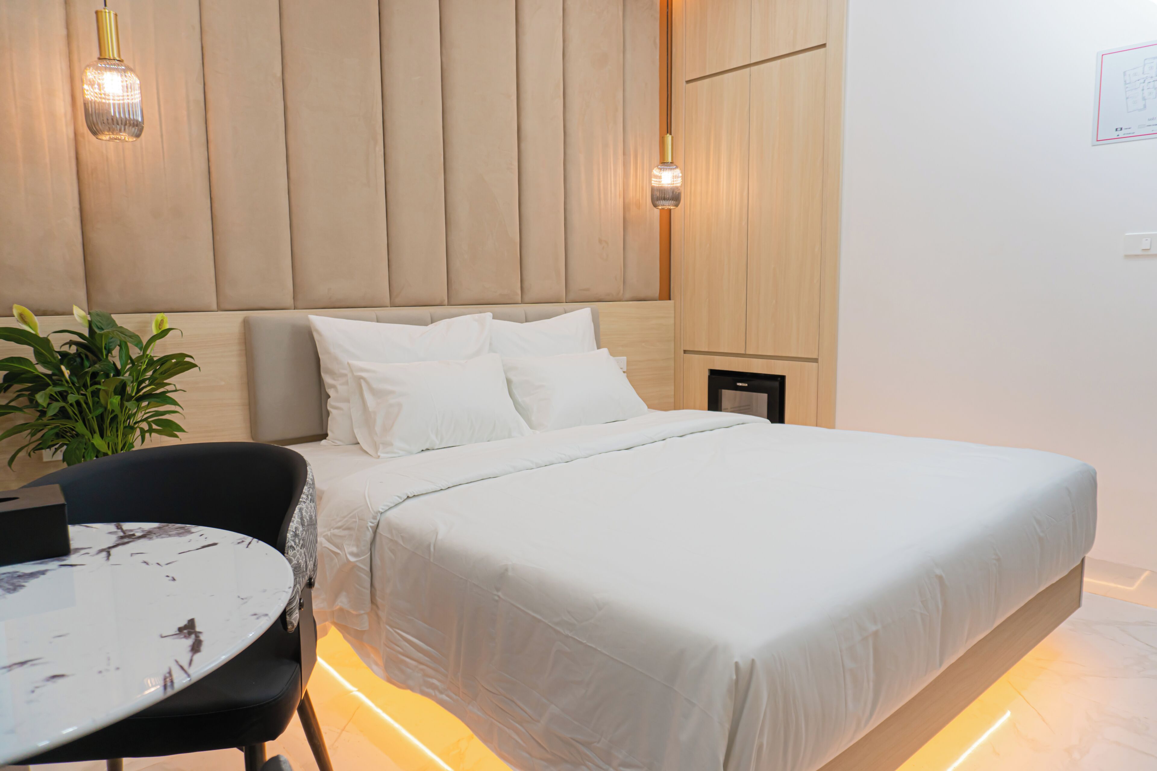 Un dormitorio moderno con una cama, mesitas de noche, una mesa redonda y una planta en maceta.