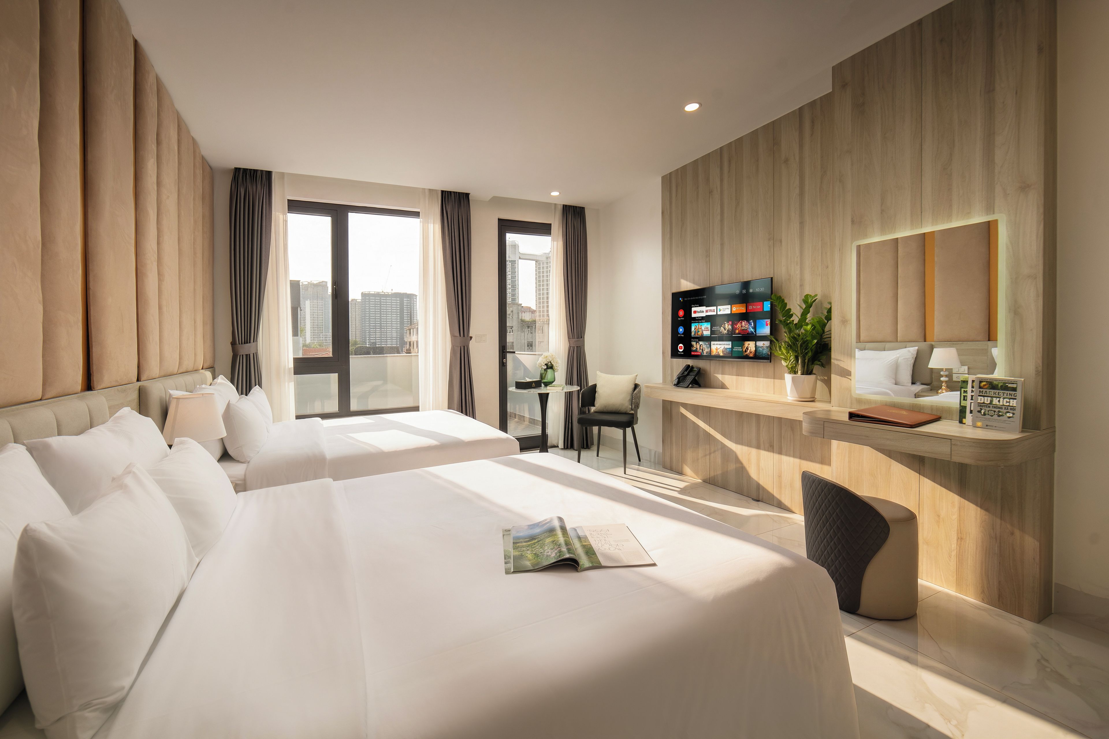 Una habitación de hotel moderna con dos camas, un escritorio, una silla, un televisor y un ventanal grande.