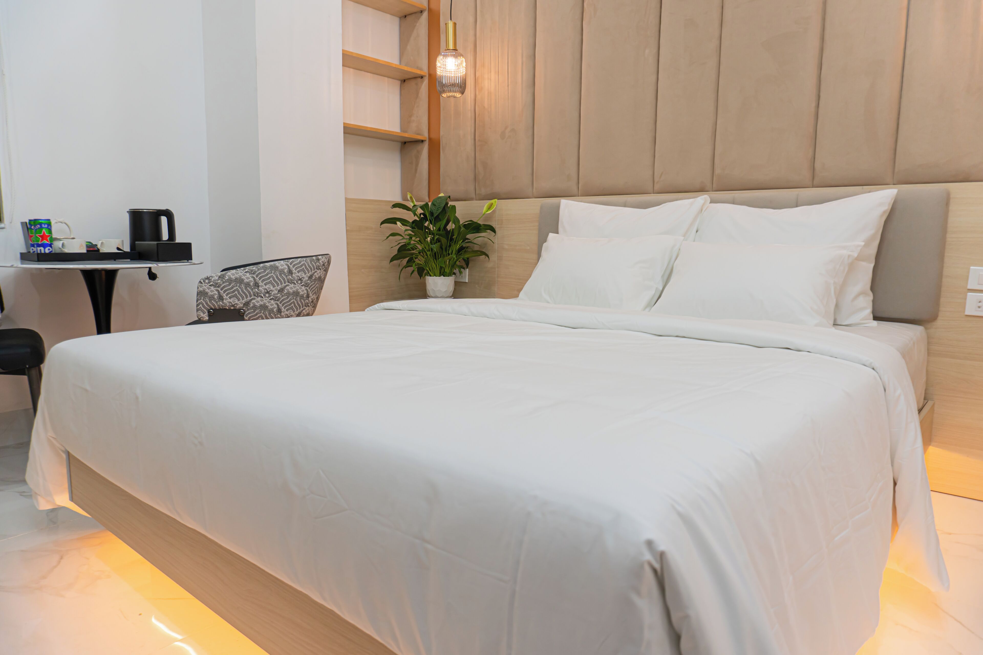 Una cama bien hecha con cabecera, una mesita de noche con lámpara y una silla.