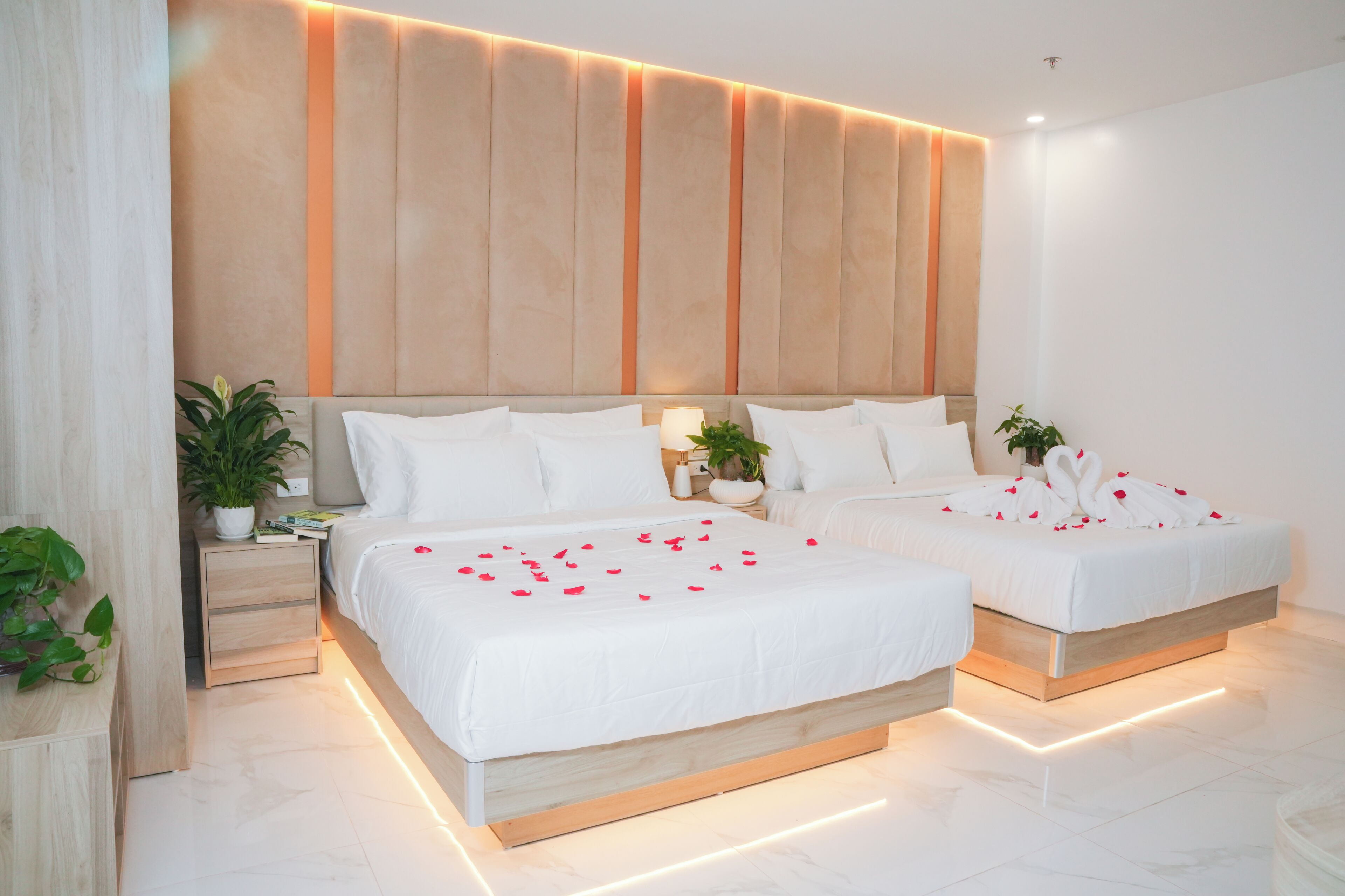 A modern hotel room with two beds, a large wall panel, and a bedside table with a plant.