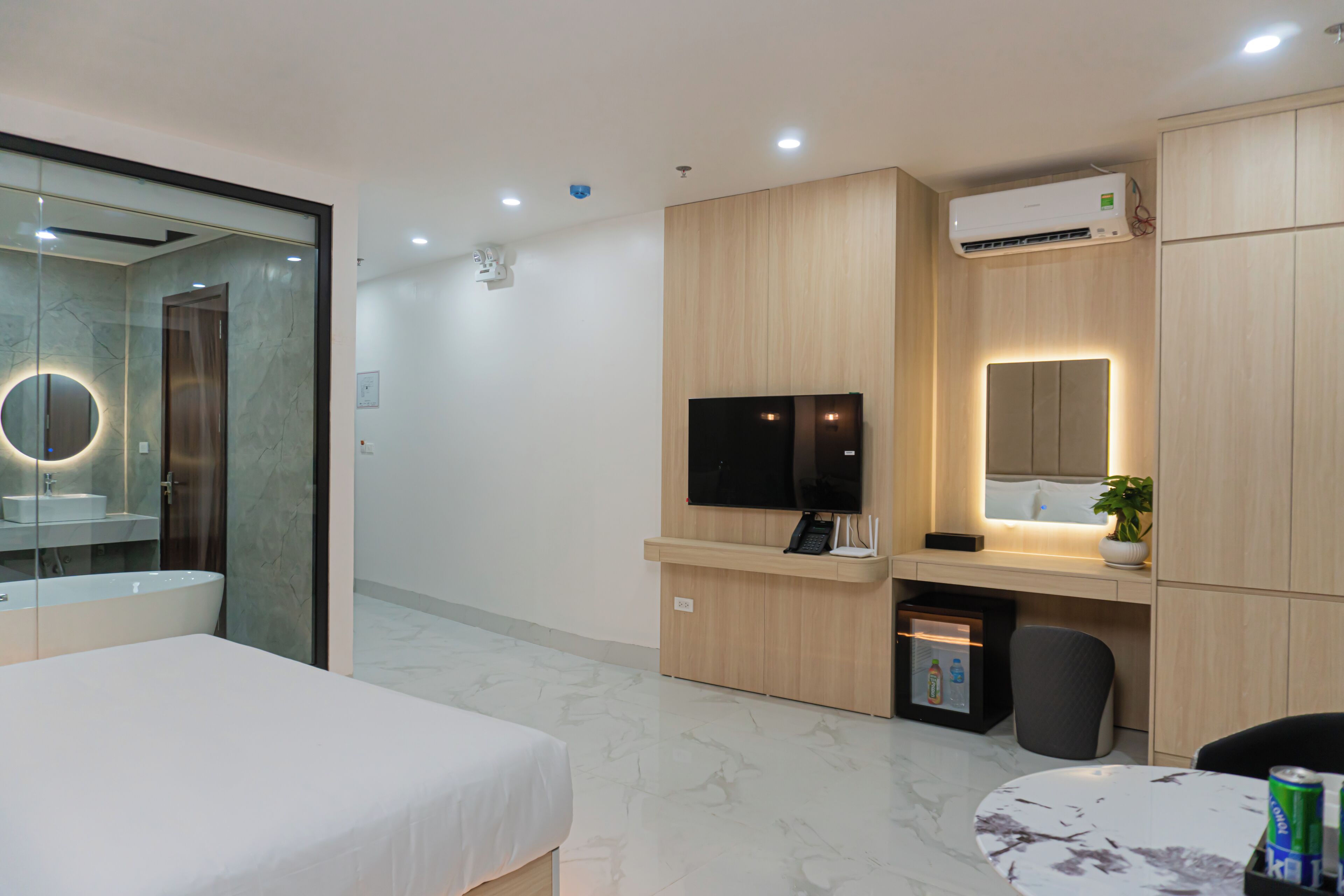 Une chambre d’hôtel moderne équipée d’un lit, d’un bureau avec un téléviseur à écran plat, d’une salle de bain avec un miroir et un lavabo, et d’un appareil de climatisation.