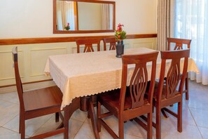 A dining area with a table set for four, wooden chairs, a vase with flowers, and a mirror on the wall.