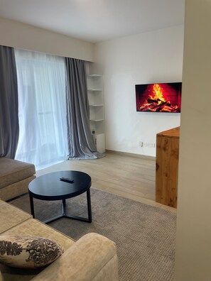 A living room with a sofa, a coffee table, a TV mounted on the wall, and a fireplace.