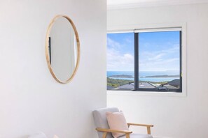 Ein Zimmer mit großem Fenster, einem spiegelnden Holzrahmen und einem grauen Sessel.