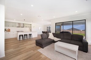 Ein modernes Wohnzimmer mit grauem Sofa, einem weißen Couchtisch und einer Küchenzeile mit weißen Schränken und einem Barhocker.