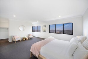 Ein modernes Hotelzimmer mit einem großen Bett, zwei Sessel, einem runden Spiegel und Blick ins Grüne durch die Fenster.