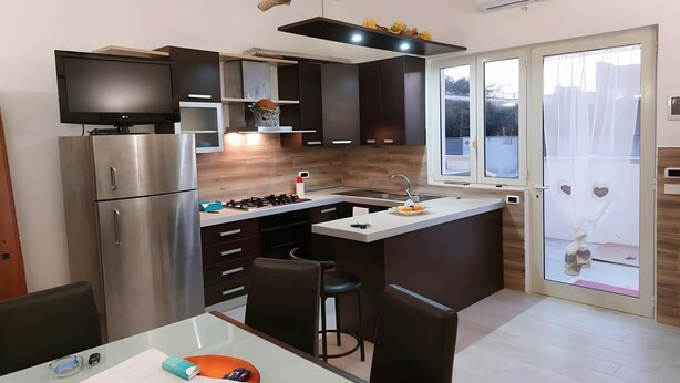 A modern kitchen with a built-in TV, a refrigerator, a stove, and a bar area. - Marylu' Holiday Home in Torre Specchia (Torre Specchia Ruggeri)