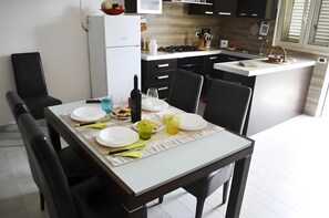 A modern kitchen with white cabinetry, a dining table set for four, and a small island with a sink. - Marylu' Holiday Home in Torre Specchia (Torre Specchia Ruggeri)