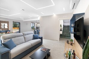 A modern living room with a sofa, coffee table, and a flat-screen TV. - Villa Elios (Massa Lubrense)