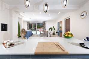 A modern kitchen with a central island, a dining area with a table and chairs, and a living room with a sofa and a TV. - Villa Elios (Massa Lubrense)