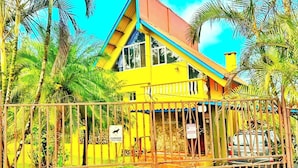 Un bâtiment jaune, doté d’une entrée fermée par un portail et entouré de palmiers.