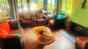 Un salon comprenant un canapé, des fauteuils, une table basse et offrant une vue dégagée grâce à de grandes fenêtres.