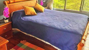 Une chambre à coucher avec un lit, une tête de lit en bois, des tables de chevet, un tapis coloré et une fenêtre donnant sur un paysage verdoyant.