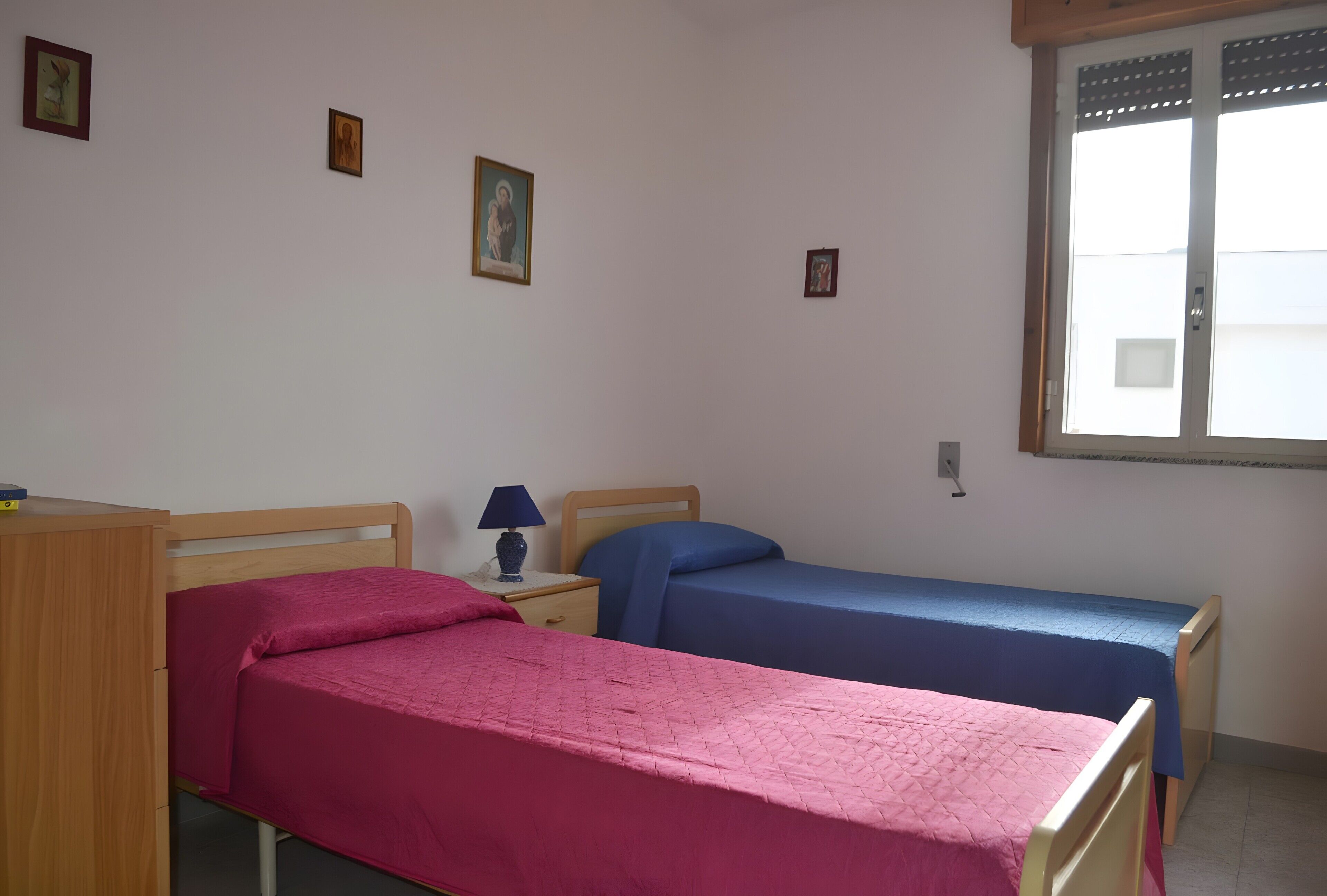 Una habitación con dos camas individuales, un escritorio de madera, una lámpara y una ventana con persianas.