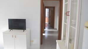 Un corridoio con un televisore su un mobile, una porta che dà su un'altra stanza e un muro rivestito di piastrelle bianche.