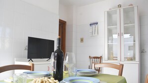 Angolo ristoro con tavolo apparecchiato per due, televisore e mobiletto con vetrine.