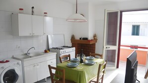 Cucina compatta con lavatrice, lavello, fornello e zona pranzo con tavolo per due persone.
