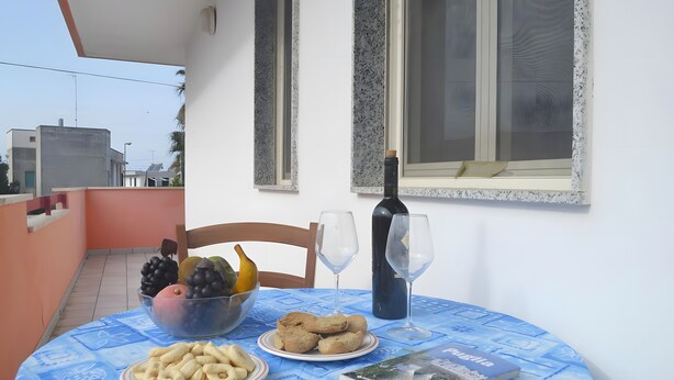 Un tavolo con una ciotola di frutta, piatti di biscotti, una bottiglia di vino e un libro su un tavolo da pranzo blu.