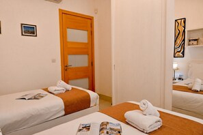Een hotelkamer met twee bedden, een houten deur, een spiegel en een klein plankje met boeken.