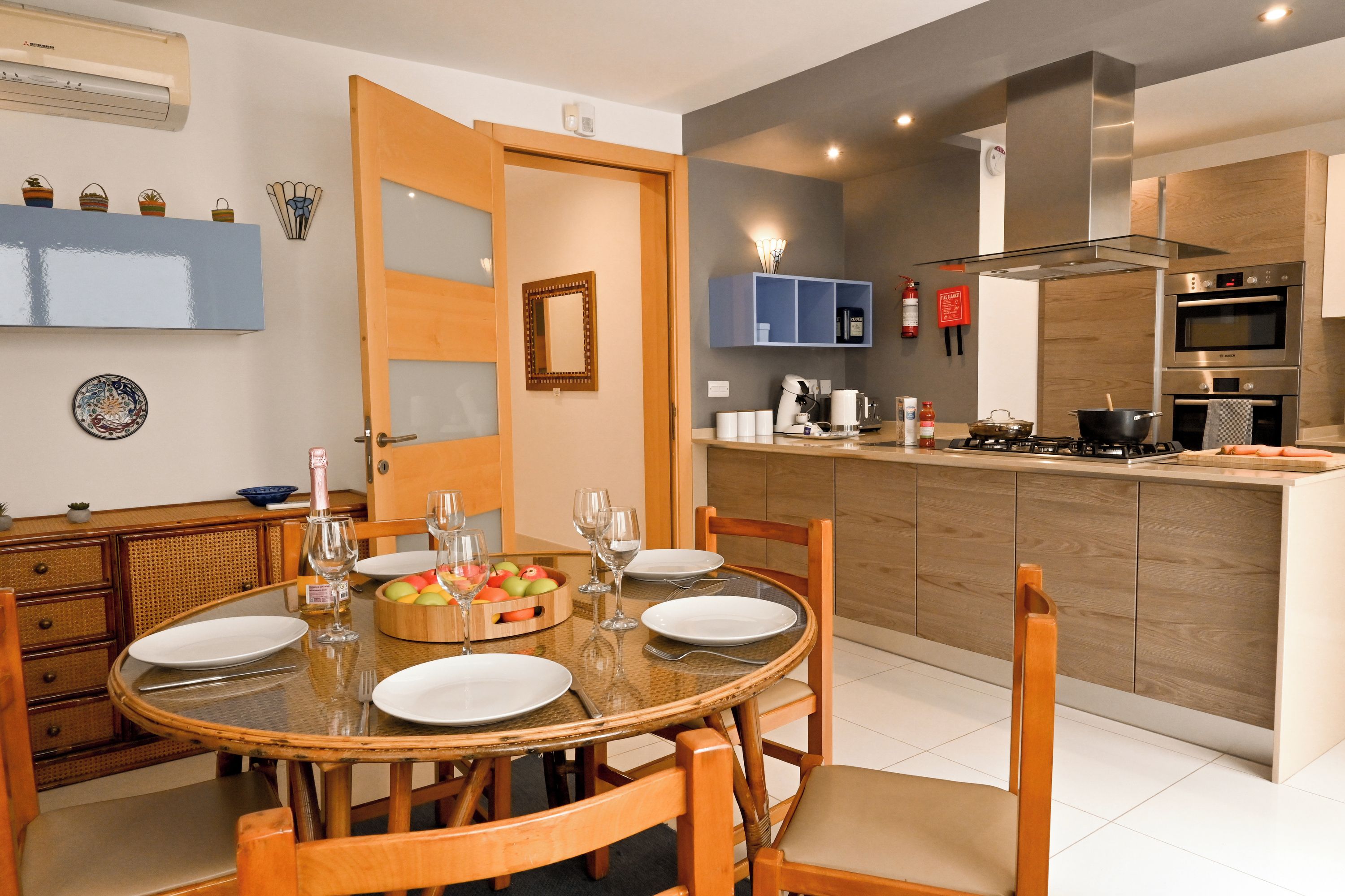 Una cocina moderna con una isla central, armarios de madera y un comedor con mesa de vidrio.