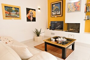 Uma sala de estar com sofá, mesa de centro, obras de arte nas paredes e lareira.