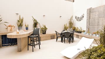 A patio area with a round table, chairs, a white lounge chair, and various potted plants.