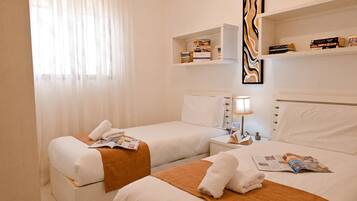 Habitación de hotel con dos camas, una mesita de noche con lámpara y un estante con libros y un objeto decorativo.