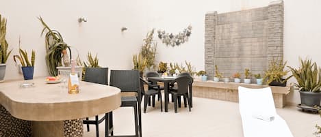 Une terrasse extérieure avec une table ronde, des chaises, un transat et diverses plantes en pot.