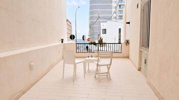 A balcony with a white table and chairs, a view of the sea, and a building in the background.