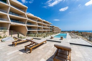 Um hotel moderno com área de piscina, várias espreguiçadeiras e vista para o oceano.