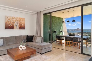 A modern living room with a sofa, coffee table, and a dining area with chairs and a table. - Luxury penthouse with stunning ocean and Arch views. Features a rooftop deck with private jetted plunge pool, grill, ping pong table, and Starlink WiFi. Near beaches, top restaurants, shopping, and Cabo nightlife for the perfect getaway. (Cabo San Lucas)