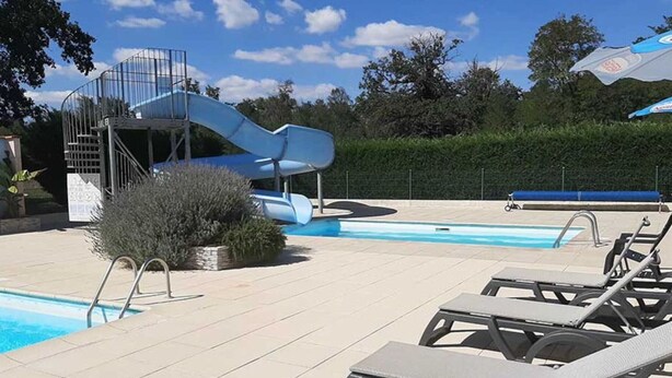 Un espace piscine doté d’un toboggan, de chaises longues et d’un ciel dégagé.