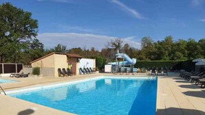 A swimming pool with lounge chairs, a water slide, and a small building. - Mobile home - 5 guests (Nonette-Orsonnette-Nonette)