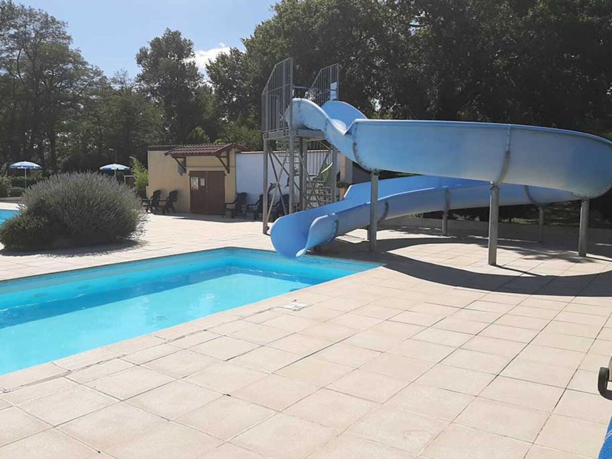 Ein Schwimmbecken mit einer blauen Rutsche und einem kleinen Gebäude im Hintergrund.