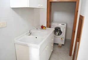 A small laundry area with a washing machine, a sink, and a plate with fruits. - Chikai Holiday Home in San Foca LL56 (San Foca)