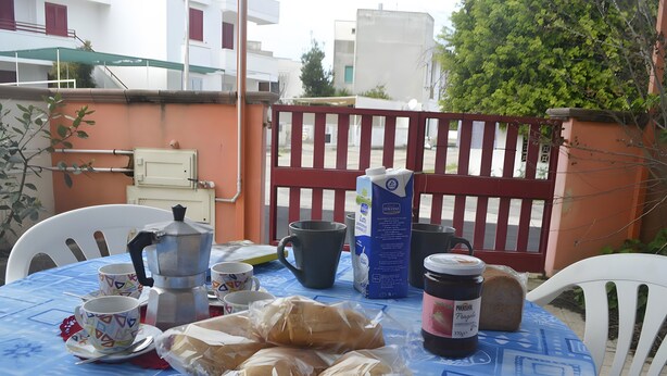 A table with a blue tablecloth, a coffee pot, cups, a plate of bread, and a juice carton. - Chikai Holiday Home in San Foca LL56 (San Foca)