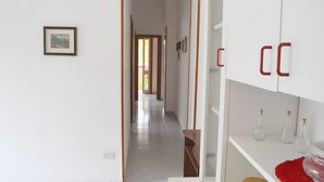 A hallway with a framed picture on the wall, a door at the end, and a white cabinet with red handles. - Chikai Holiday Home in San Foca LL56 (San Foca)