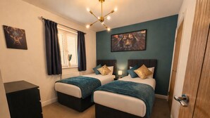 A room with two beds, a desk, a window with curtains, a ceiling light fixture, and a painting on the wall. - Central Bridgnorth Boutique Townhouse - Private Parking (Bridgnorth)