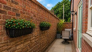 A narrow brick wall with two black flower boxes containing green plants and red berries. - Central Bridgnorth Boutique Townhouse - Private Parking (Bridgnorth)