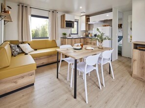 Un espace de vie moderne avec un canapé jaune, des chaises blanches, une table à manger en bois et un coin cuisine.