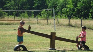 Leikkipuistossa oleva keinulauta, jonka päällä istuu kaksi lasta.