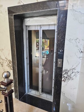 Un ascenseur en marbre avec une porte en verre, une rampe métallique et une petite sphère décorative.