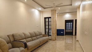 A living room with a beige sofa, a ceiling fan, and a door with a window. - Fortune Suites (Puducherry)