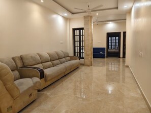 Un salon avec un canapé beige, un ventilateur de plafond et une porte avec une fenêtre.