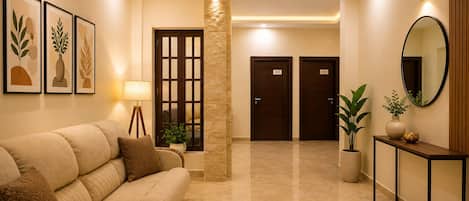 A hotel lobby with a sofa, a lamp, framed artwork, a pillar, a mirror, and two doors.