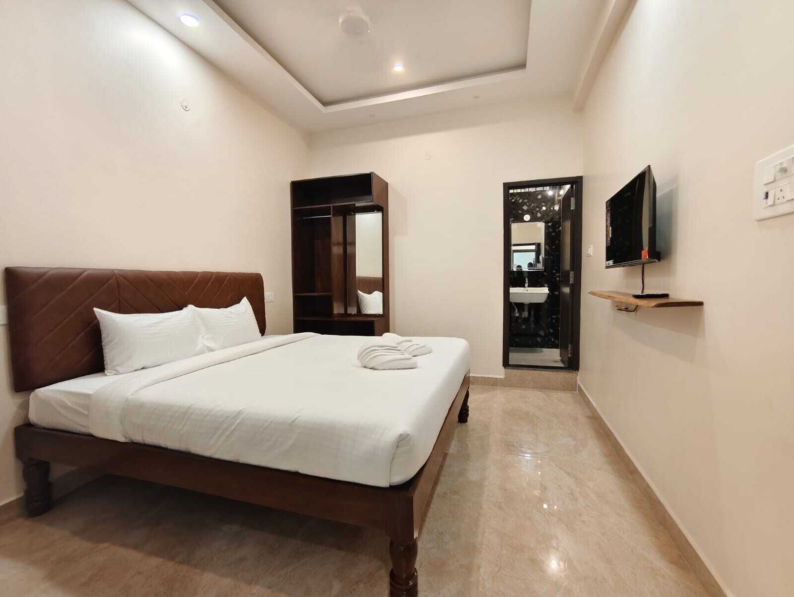 Une chambre d’hôtel avec un lit, une armoire, une télévision et une salle de bain visible à travers une porte ouverte.